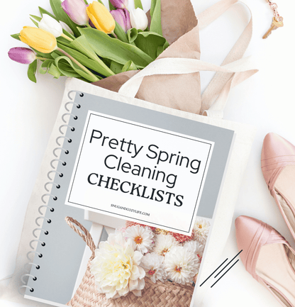 A bundle of colorful tulips wrapped in paper, a notebook with the words &quot;Pretty Spring Cleaning Checklists&quot;, and a pair of shoes sit on a table. 